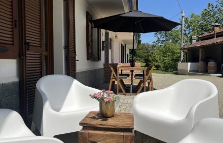 Angolo salotto con comode poltrone e ombrellone sulla terrazza de La Cascina. Set da pranzo con ombrellone sullo sfondo 