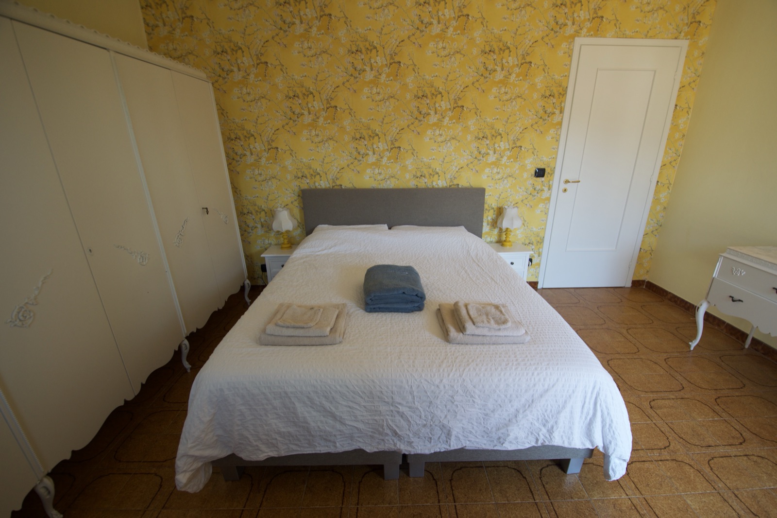 Tweepersoonsbed in een slaapkamer van La Cascina met warme gele accentmuur